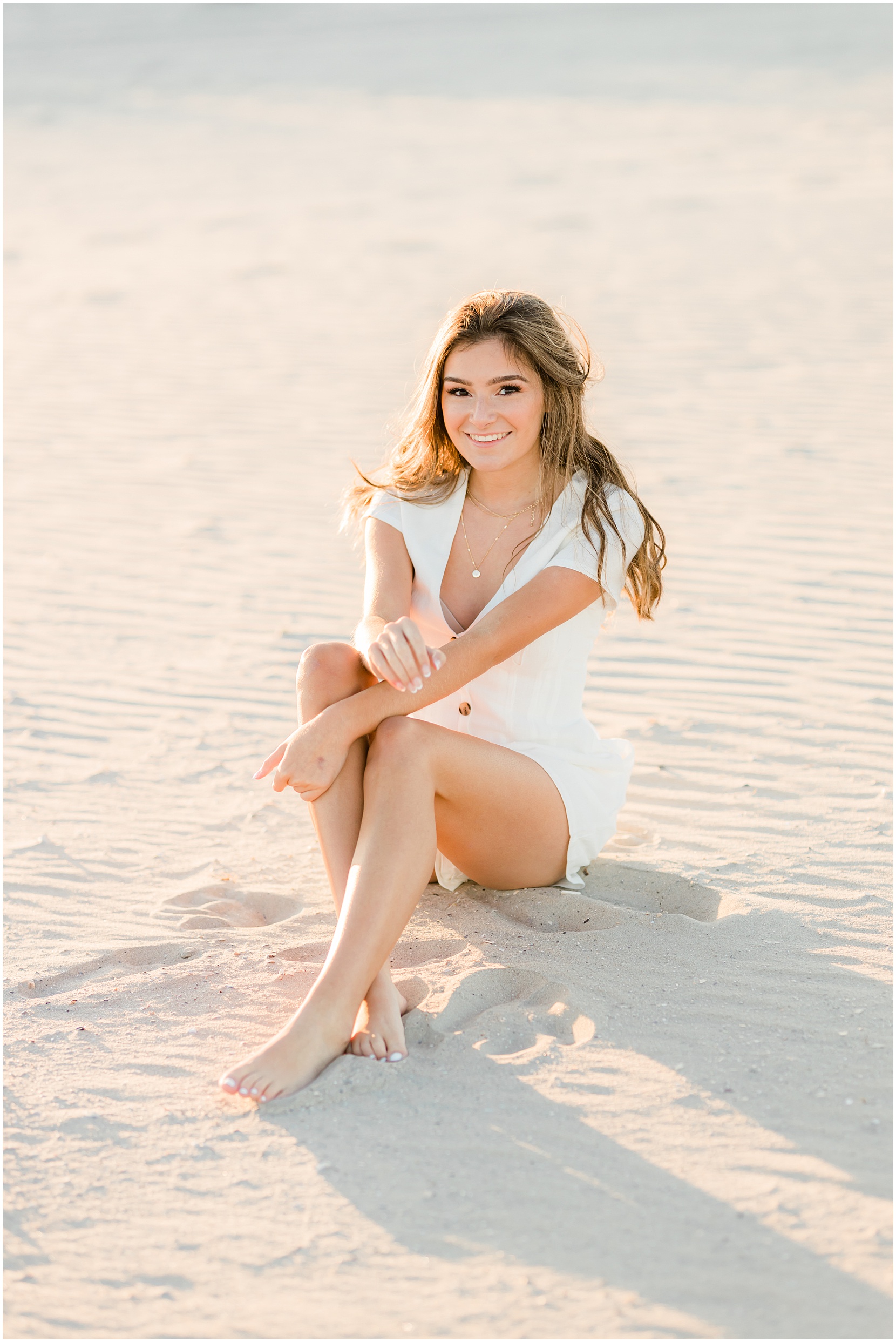 Teen girl posing for her senior pictures with Nicole Marie Photography. She is sitting in the golden sun on the beach in Ocean City New Jersey.