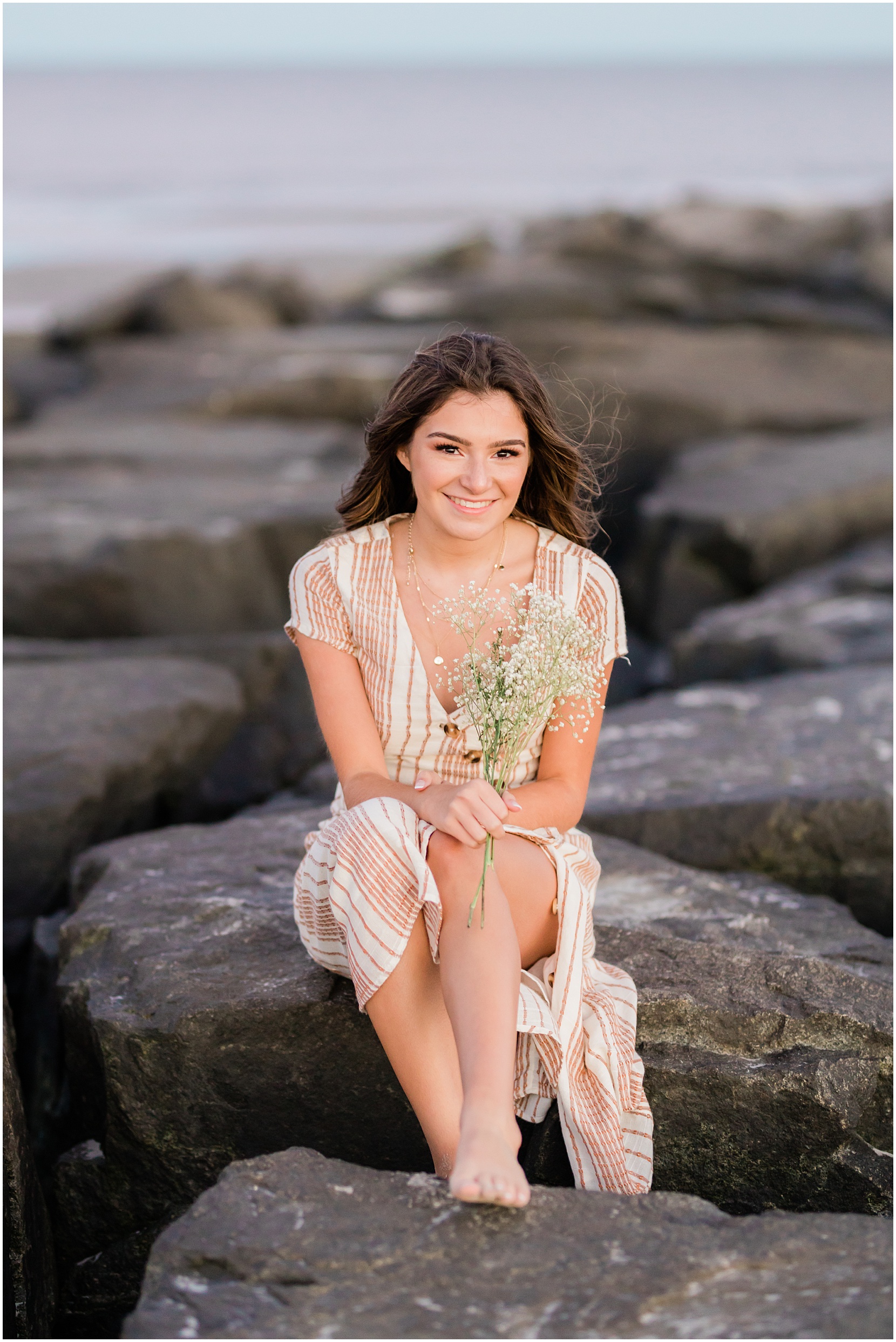Teen girl posing for her senior pictures with Nicole Marie Photography. She is standing in the under the pink sunset sky in Ocean City New Jersey. She is posing on the jetty.